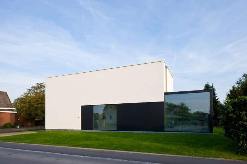 Modern minimalist house with clean lines and geometric design, featuring white and black façade, large glass windows, and surrounding green lawn, showcasing contemporary architecture style.
