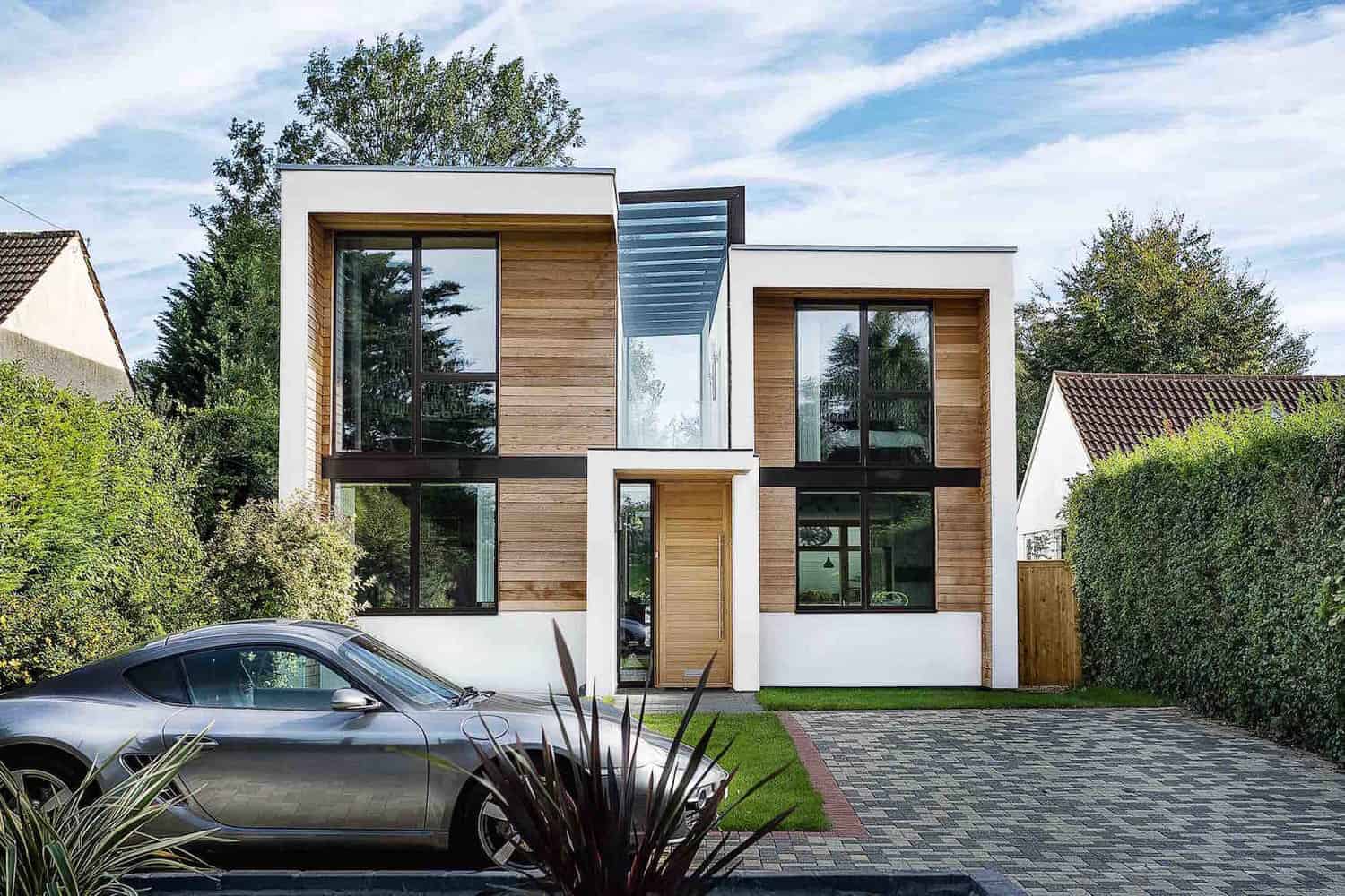 Contemporary modern house with wooden and white facades, large glass windows, and sleek architectural design, featuring eco-friendly curb appeal, surrounded by greenery and a stylish driveway.