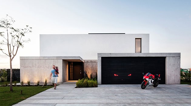 Modern minimalist house with sleek concrete facade and black garage door, featuring sharp architectural lines and contemporary design elements.