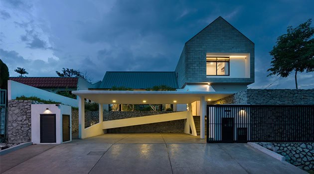 Modern minimalist house with sleek concrete and stone facade, illuminated exterior lighting, and contemporary architectural design, set against a backdrop of a cloudy evening sky.