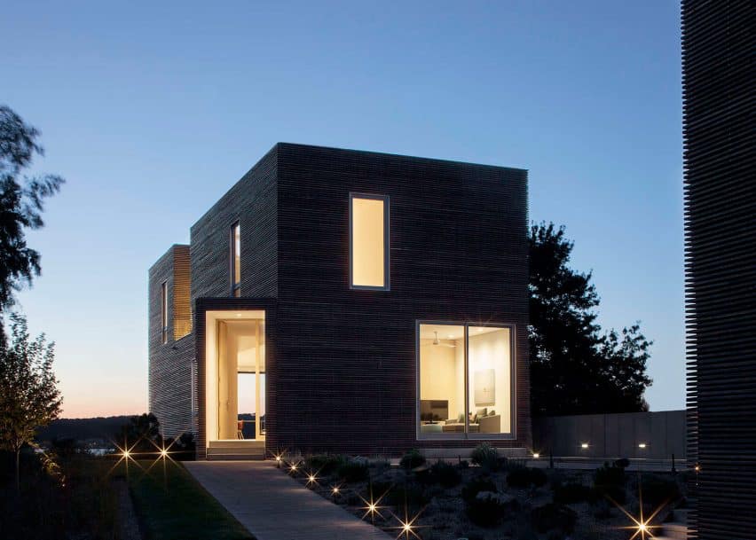 Contemporary modern black house with large windows and minimalist design during evening with outdoor lighting and natural surroundings.