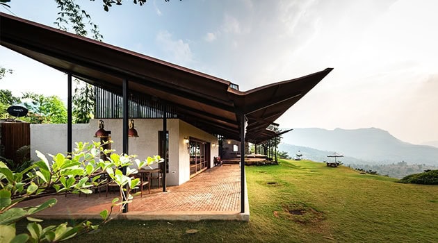 Modern hillside house with expansive glass windows, sloped roof design, and surrounding lush green landscape, ideal for luxury outdoor living and scenic mountain views.