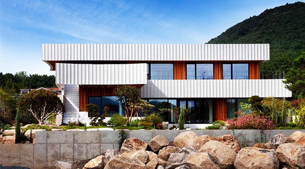 Contemporary modern house with sleek white exterior, large glass windows, and surrounding lush landscape in a mountain setting.