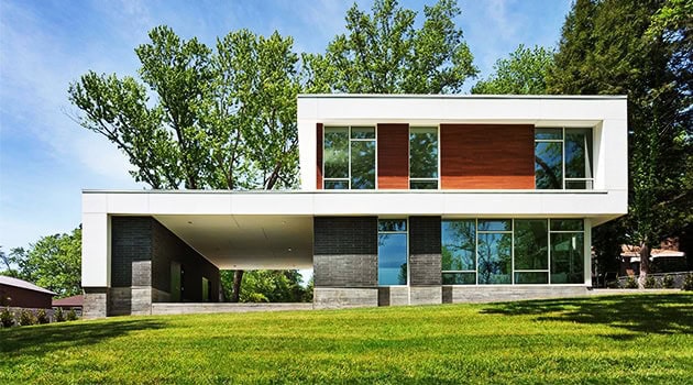 Sleek modern house with minimalist architecture, featuring large glass windows, clean lines, and a flat roof amidst lush green surroundings.