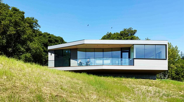 Modern minimalist glass house on a hillside with sleek architectural design and panoramic views, highlighting contemporary architecture and innovative building styles.