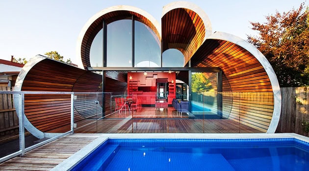 Sustainable futuristic house with stacked, shell-like wooden structures, large glass windows, and a private pool, blending modern architecture with innovative design.