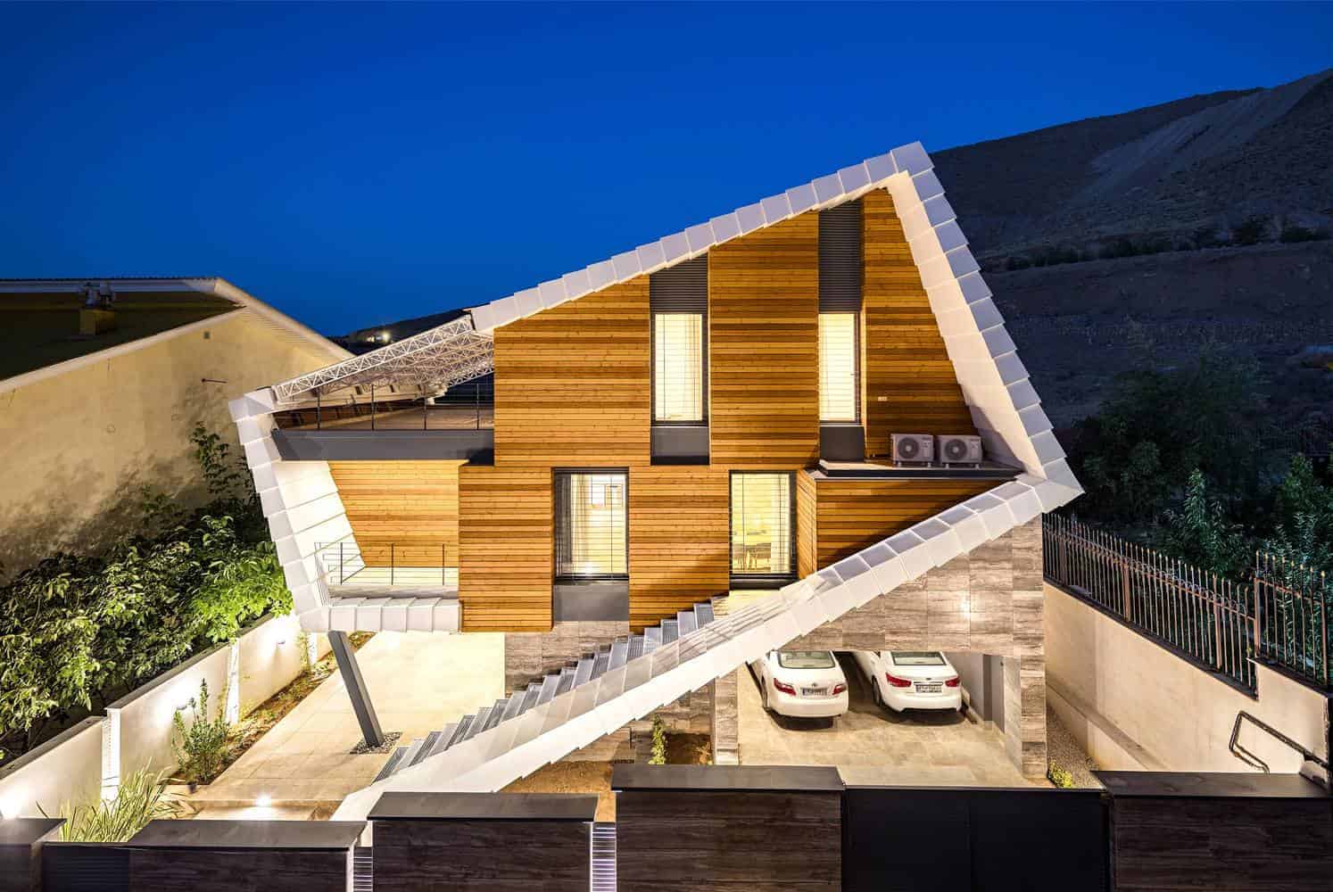 Modern mountain house with unique angular architecture and wooden accents at dusk, featuring a spacious garage and outdoor lighting, exemplifying innovative residential design.