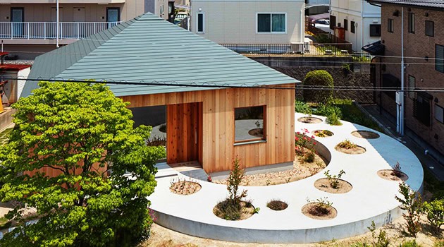 Modern residential backyard landscape with unique wooden structure, curved concrete pathway, and minimalist plant design, showcasing contemporary architecture and outdoor design.