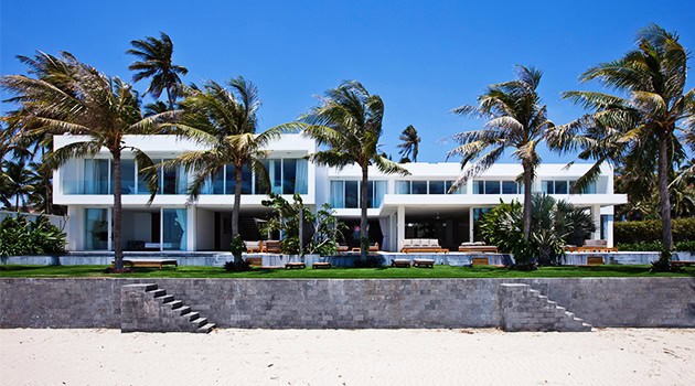 Luxurious modern beachfront house with sleek architectural design, surrounded by palm trees and ocean views, exemplifying contemporary architecture and elegant outdoor living.