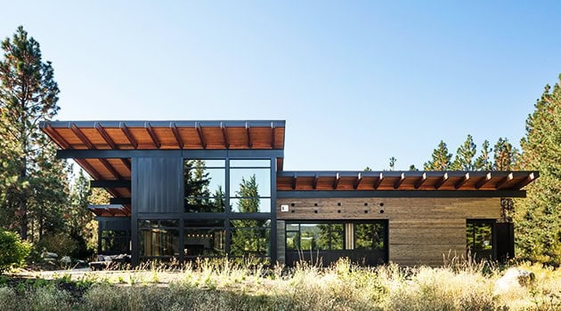Modern contemporary house design with large glass windows and wooden accents in a natural landscape setting.