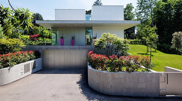 Modern minimalist house with clean lines and a spacious garage, surrounded by lush landscaping and vibrant plants, showcasing contemporary architectural design and outdoor garden integration.