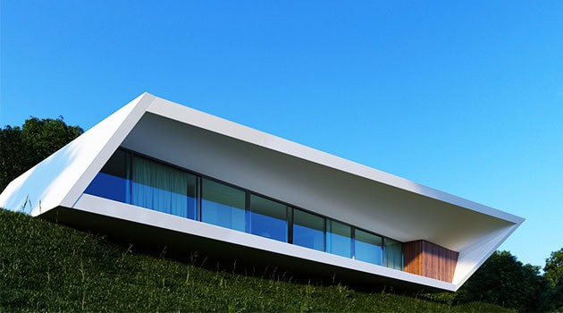 Futuristic modern house with sleek white exterior and large glass windows on a green hillside under a bright blue sky.