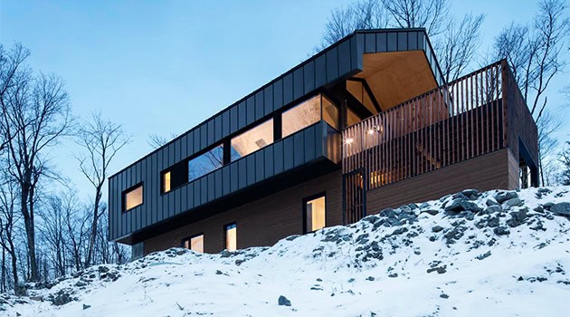 Contemporary modern house with sleek black exterior and large windows nestled in snowy landscape, showcasing innovative architecture design.