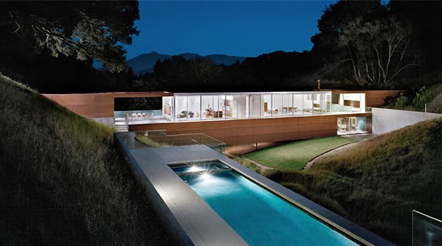 Modern luxury hillside mansion with a sleek outdoor infinity pool and contemporary glass architecture at night.