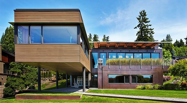 Contemporary modern house with large glass windows, wooden and metal exterior, situated in lush green surroundings, showcasing innovative architecture and design.