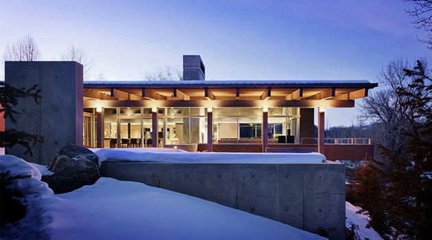 Sustainable modern house with large glass windows and flat roof design in a winter landscape.