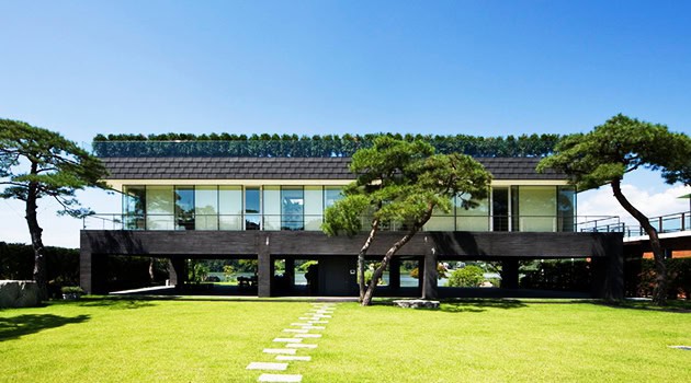 Modern minimalist black and glass house with open plan design surrounded by lush green lawn and mature trees, showcasing contemporary architecture and innovative home design.