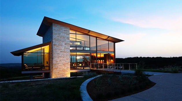 Modern glass and stone architectural house illuminated at dusk, showcasing contemporary design and innovative architectural elements.