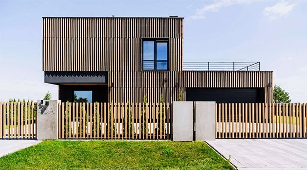 Sustainable modern wooden house with minimalist design and sleek fencing, showcasing innovative architecture and eco-friendly building materials.