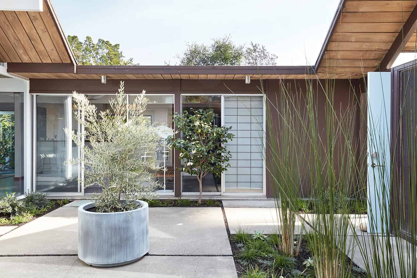 Modern minimalist house courtyard with outdoor plants, concrete paving, and large glass sliding doors, emphasizing contemporary architecture, outdoor living, and sleek design elements.
