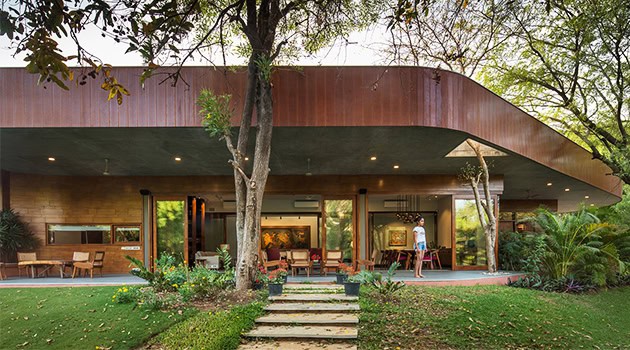 Modern contemporary house with sleek architectural design featuring wood and glass elements in a lush garden setting. Open-plan living space seamlessly blending indoor and outdoor environments.