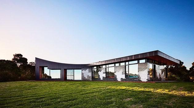 Sleek modern architectural house with curved design, large glass windows, and minimalist style, set in a lush green landscape, showcasing innovative contemporary architecture and design.