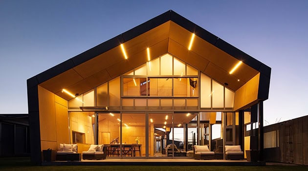Modern contemporary house with expansive glass walls and a striking peaked roof, showcasing innovative architecture and sleek design at sunset.