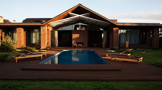 Modern brick house with a sleek backyard pool, wooden deck, and outdoor lounge chairs showcasing contemporary architecture and luxurious outdoor living spaces.