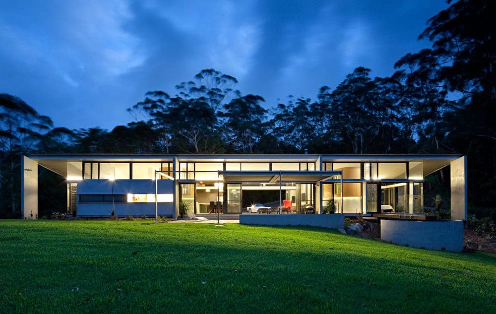 Contemporary modern house with large glass windows, minimalist design, and eco-friendly architecture nestled in lush greenery at dusk.