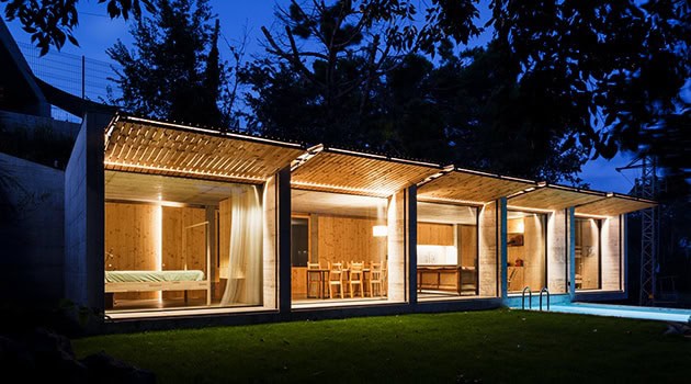 Modern minimalist glass house with wooden accents and outdoor pool at night, showcasing contemporary architectural design and sleek interior living spaces.