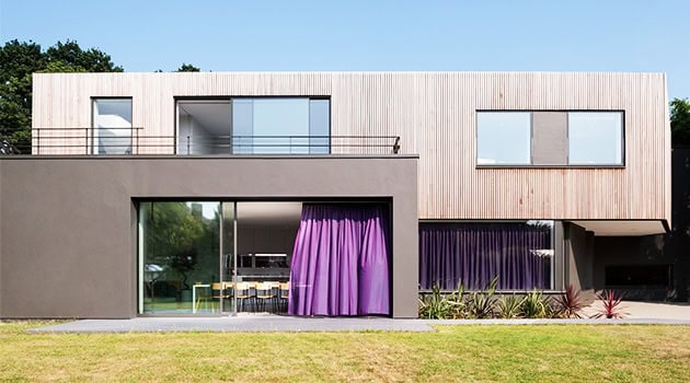 Modern minimalist house with large glass windows and vibrant purple curtains, showcasing contemporary architecture and innovative design elements.