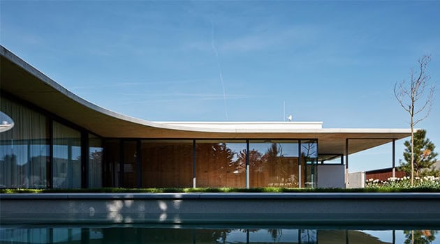 Modern minimalist house with curved roof and large glass windows, showcasing contemporary architecture design and eco-friendly materials.