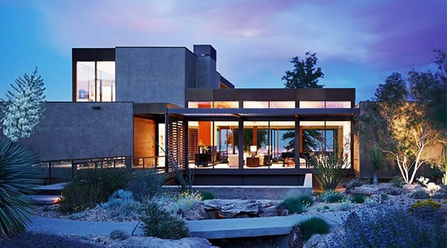 Contemporary modern luxury house with extensive glass windows, minimalist design, and desert landscaping under twilight sky.