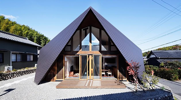 A-frame modern house with black metal roofing, large glass windows, and wooden accents, situated in a serene suburban neighborhood.