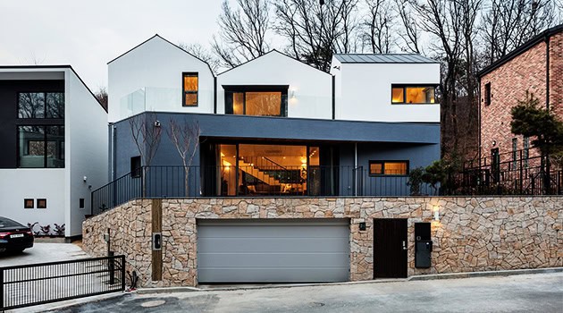 Contemporary modern house with geometric design, white and dark exterior, large glass windows, stone accents, and a landscaped front yard in an upscale neighborhood.