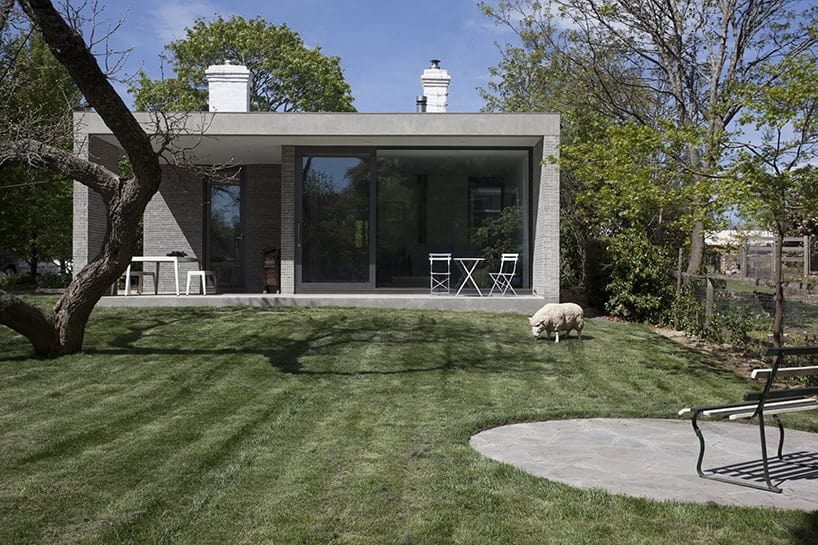 Modern minimalist house with large glass sliding doors and a landscaped garden with a sheep grazing.