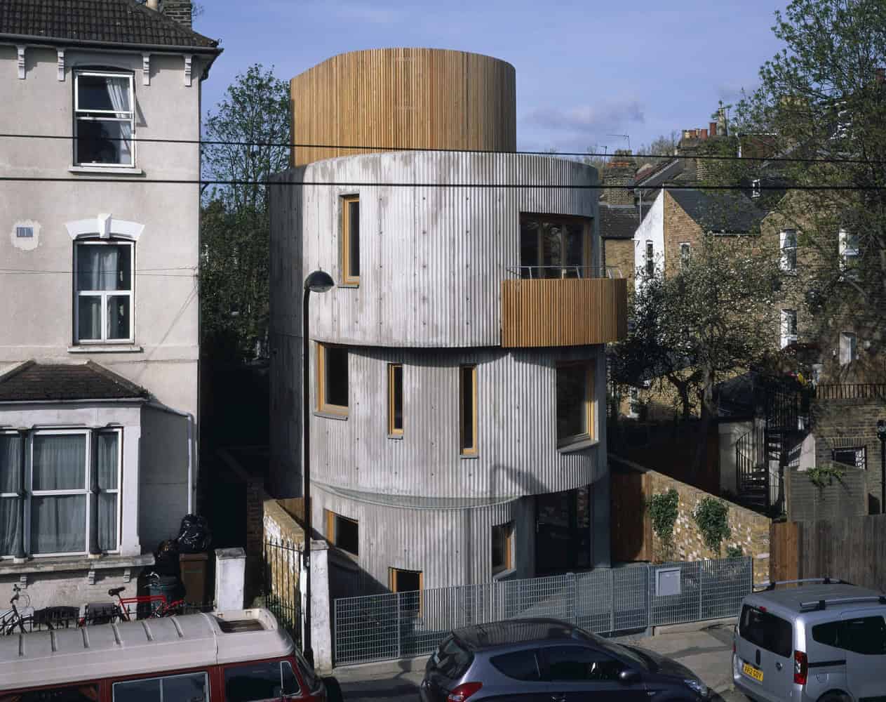 Contemporary cylindrical wooden house with modern architecture, mixed with urban residential environment, featuring unique rounded design and natural wood exterior.