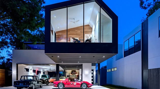 Luxury modern house with glass facade and garage displaying vintage cars, contemporary architectural design, sleek lines, innovative structure, and stylish interior lighting.
