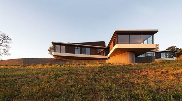 Sleek modern house with large glass windows and innovative architectural design on a grassy landscape.