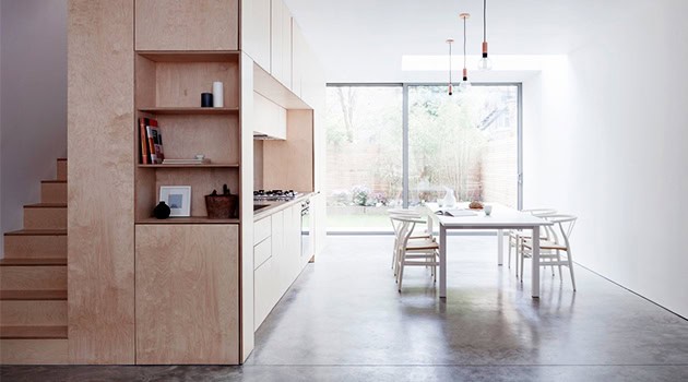 Modern minimalist kitchen and dining area with natural wood cabinetry, spacious layout, and large glass sliding doors offering plenty of natural light.