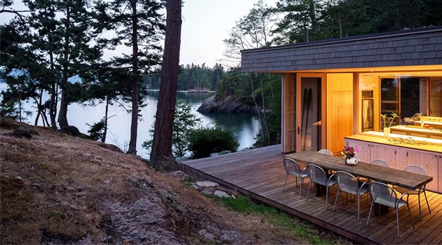 Secluded modern lakeside cabin with expansive wooden deck surrounded by lush forest and overlooking a tranquil lake, perfect for nature-inspired architecture and outdoor living.