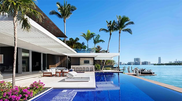 Luxurious waterfront modern villa with infinity pool, sleek outdoor lounge area, and tropical palm trees, showcasing contemporary architecture and design for a sophisticated coastal living experience.