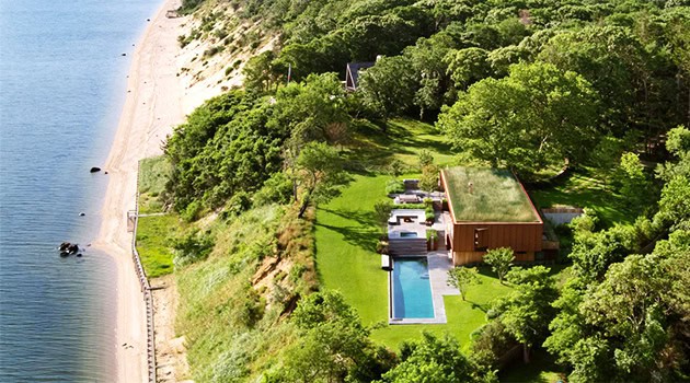 Luxury modern house with pool overlooking the coast surrounded by lush greenery and trees, emphasizing luxury waterfront architecture and contemporary design elements.