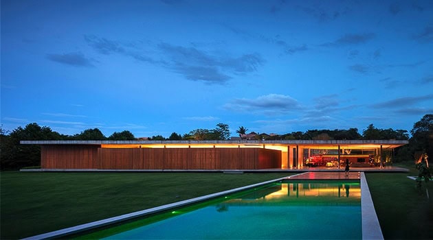 Sleek modern house with minimalist design, illuminated exterior at dusk, lush green lawn, and infinity pool, showcasing contemporary architecture and innovative outdoor living spaces.