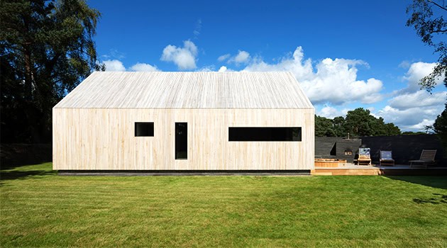 Modern minimalist wooden house with clean lines and expansive windows in a lush green landscape, showcasing contemporary architecture and innovative design.