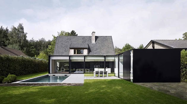Modern minimalist house with sleek glass walls and a swimming pool, surrounded by lush greenery in a contemporary architectural design.