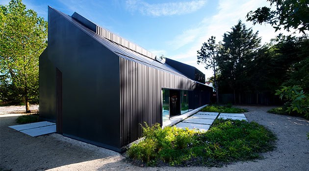 Modern black metal residential building with sleek architectural design and large windows, surrounded by greenery and outdoor pathway, showcasing contemporary architecture and innovative home design.