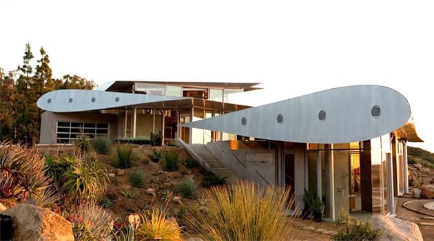 Futuristic modern house with sleek architectural design and curved metallic accents, set amidst desert landscaping.
