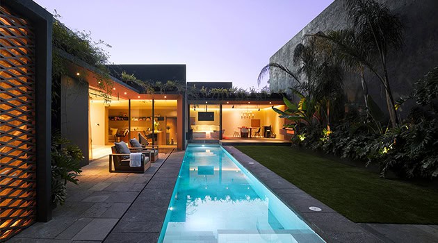 Sleek modern backyard with illuminated indoor-outdoor living spaces, pool, and lush landscaping, showcasing contemporary architecture and outdoor design elements ideal for luxury home environments.