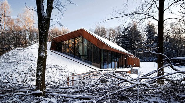 Modern snow-covered wooden house with large glass windows nestled in winter landscape.